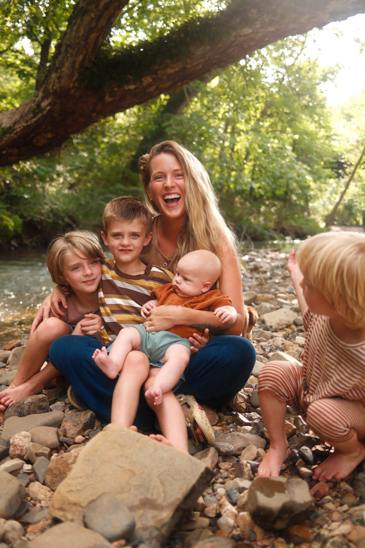 Taylor laughing with her children by a creek in the woods.